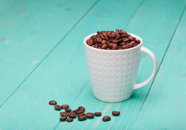 Vacker vit kaffekopp med kaffebönor på trä turkos bakgrund — Stockfoto