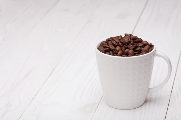 Beautiful white coffee cup with coffee beans on wooden background — Stock Photo, Image