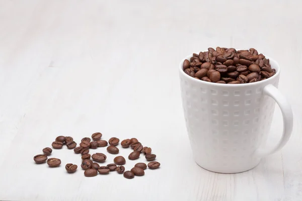 Beautiful white coffee cup with coffee beans on wooden background — Stock Photo, Image