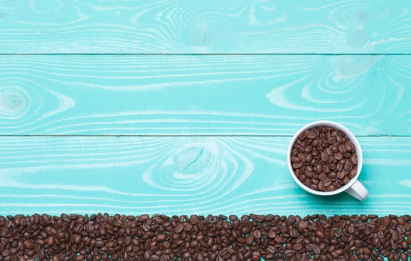 Красива біла чашка кави з кавовими зернами на бірюзовому дерев'яному фоні — стокове фото