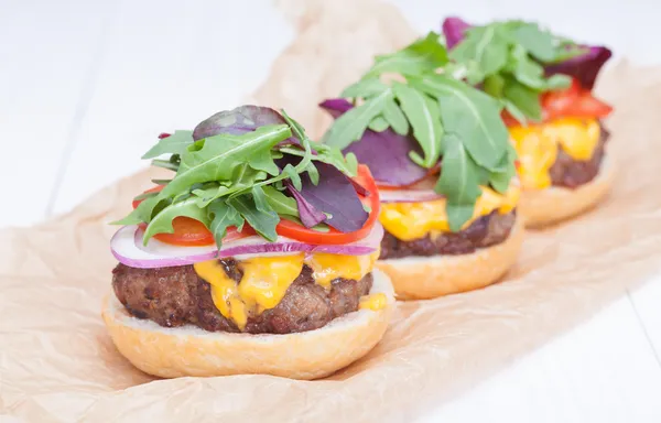 Hamburgers pepper cheese onions sauce tomatoes on paper — Stock Photo, Image