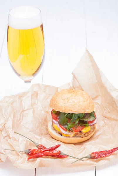 Hamburger cheese onions sauce tomatoes on paper and beer — Stock Photo, Image