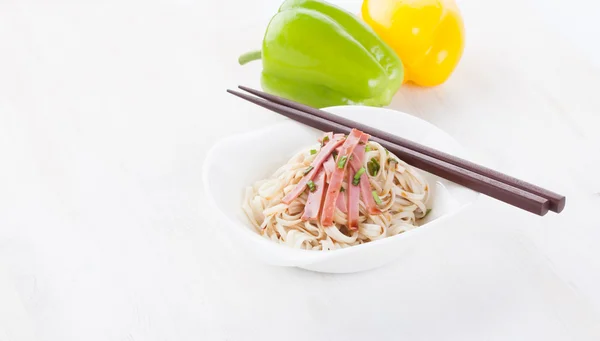 Leckere Nudeln mit schinken grünen Zwiebeln in einer schönen weißen Schüssel auf weißem Holzgrund. Paprika und Tomaten. — Stockfoto