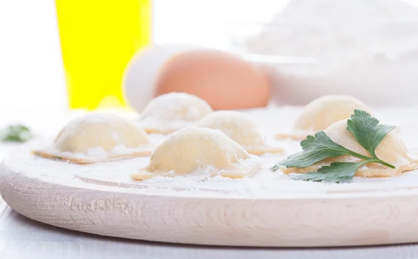 Homemade ravioli on a round wooden board and egg flour oil parsley — Stock Photo, Image