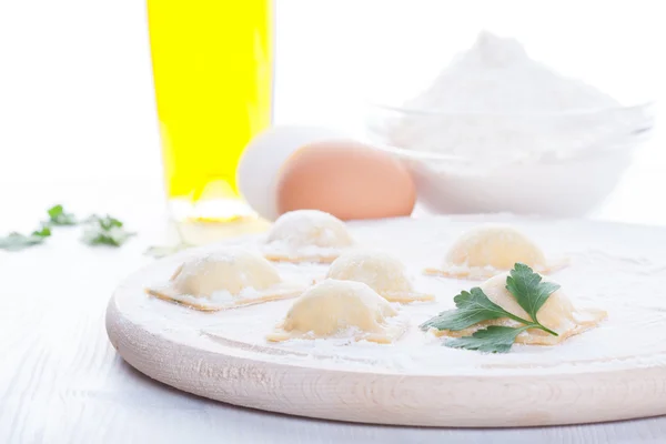 Homemade ravioli on a round wooden board and egg flour oil parsley — Stock Photo, Image