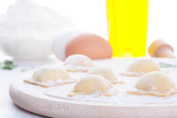 Homemade ravioli on a round wooden board and egg flour oil parsley — Stock Photo, Image