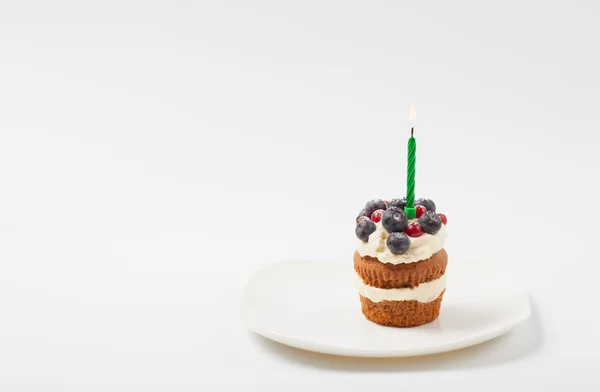 Sabroso hermoso pastel de frutas con crema y bayas en un plato con una vela — Foto de Stock