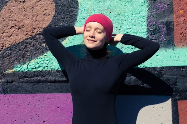 Девушка в черных солнечных ваннах у разноцветной стены в красной шапке — стоковое фото