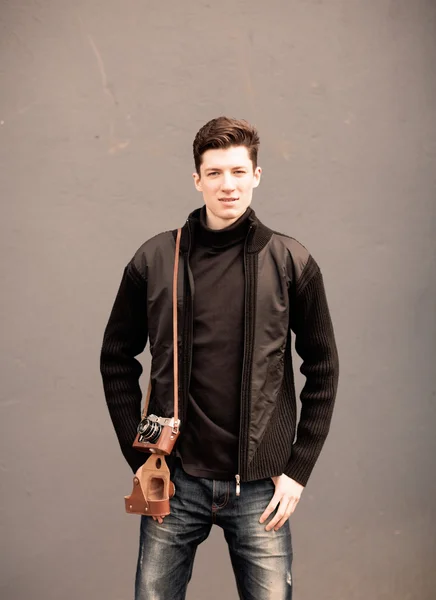 Mladý muž model představuje na zeď s vinobraní fotoaparát na rameni — Stock fotografie