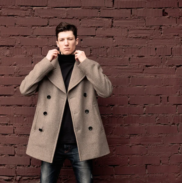 The young man model in a coat poses at a brick wall. Toned — Stock Photo, Image