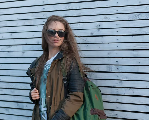 Menina bonita Cabelo longo. Casaco de turista, mochila. parede de madeira branca . — Fotografia de Stock