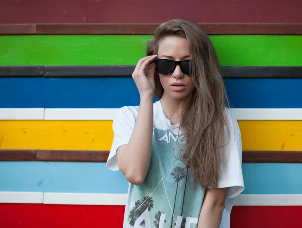 La hermosa joven con el pelo largo en gafas de sol en una pared multicolor —  Fotos de Stock