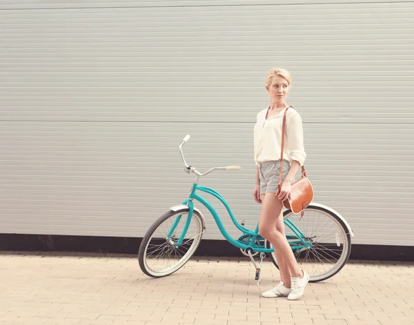 Bella ragazza bionda è in piedi vicino alla bicicletta vintage con borsa vintage marrone, caldo, tonificante — Foto Stock