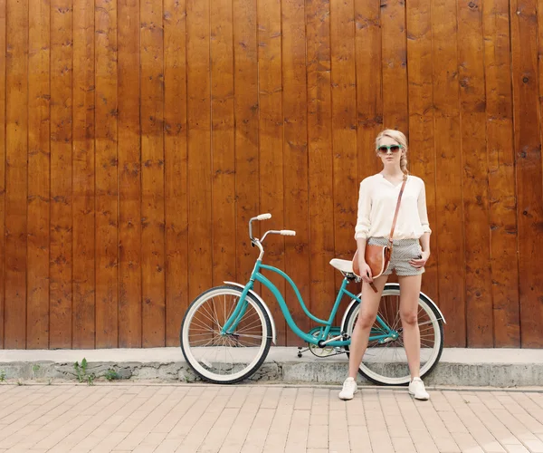 Giovane ragazza bionda sexy con i capelli lunghi in occhiali da sole verdi in piedi vicino bicicletta verde vintage divertirsi e buon umore guardando in macchina fotografica e sorridente, caldo, tonificante — Foto Stock