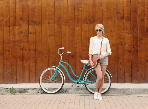 Menina loira sexy nova com cabelos longos em óculos de sol verdes de pé perto da bicicleta verde vintage se divertir e bom humor olhando na câmera e sorrindo, quente, tonificação — Fotografia de Stock