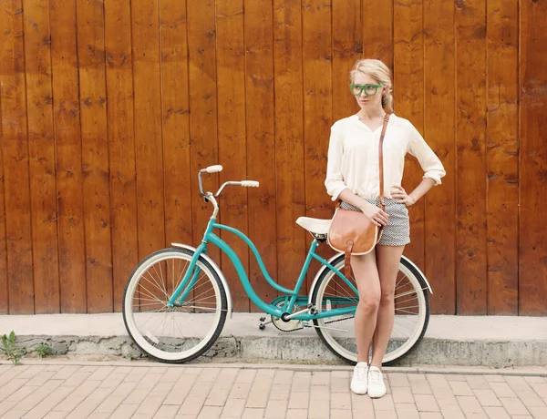 Young sexy blonde girl is standing near the vintage green bicycle with brown vintage bag in green sunglasses, warm, tonning — Stock Photo, Image