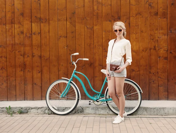 Menina loira sexy nova está de pé perto da bicicleta verde vintage com câmeras vintage marrom em óculos de sol laranja., quente, tonificação — Fotografia de Stock