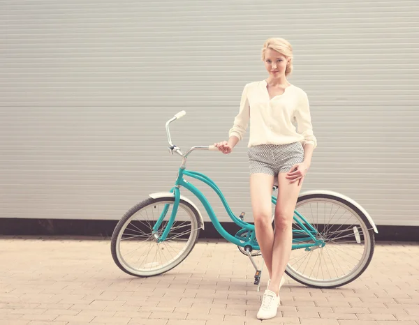 Hermosa chica rubia está de pie cerca de la bicicleta vintage divertirse y buen humor mirando en la cámara y sonriendo, cálido, tonificación —  Fotos de Stock