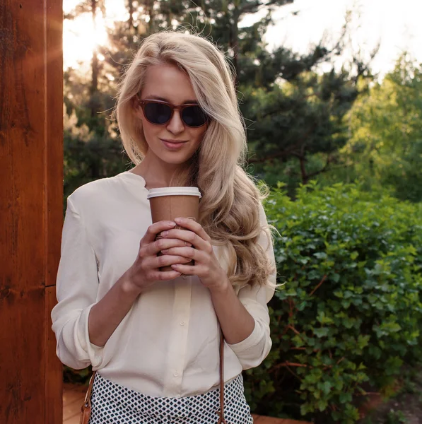 Jonge sexy blonde meisje met lange haren in zonnebril houden een kopje koffie veel plezier en goed humeur op zoek in de camera en glimlachend, warm, tonning — Stockfoto