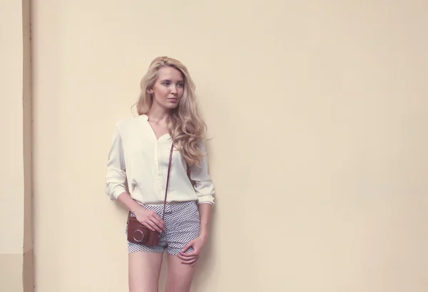 Schöne sexy blonde Frau mit langen Haaren posiert an der Wand mit Vintage-Kamera, warm, Tonning — Stockfoto