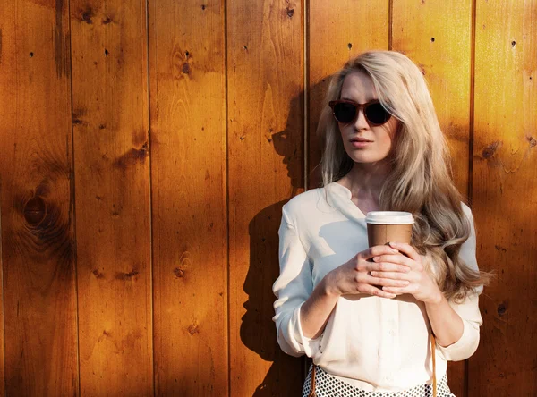 Menina loira sexy nova com cabelos longos em óculos de sol segurando uma xícara de café divirta-se noite luz solar macia, quente, tonificação Imagem De Stock