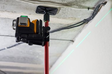 İnşaat alanındaki duvarda yeşil lazer ışını olan lazer seviyesi ölçüm aracı. Ölçüm seviyesi. Uzatma tavanı için profesyonel ekipman. Ev yenileme konsepti, kapatın.