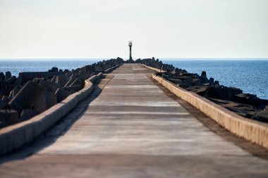 Avrupa 'da bir yerde işaret feneriyle güçlendirilmiş boş beton iskele, kopyalama alanı. Dalgalar kapanıyor, açık mavi gökyüzü, deniz manzarası, güzel sakin mavi deniz arka planı.