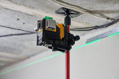 İnşaat alanındaki duvarda yeşil lazer ışını olan lazer seviyesi ölçüm aracı. Ölçüm seviyesi. Uzatma tavanı için profesyonel ekipman. Ev yenileme konsepti, kapatın.
