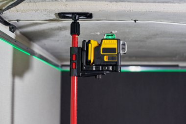 Tamamlanmamış dairede duvarda yeşil lazer ışını olan lazer seviyesi ölçüm aracı. Uzatma tavanı için profesyonel ekipman. Ev yenileme konsepti, kapatın.