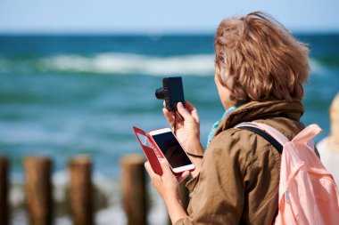Kahverengi saçlı kadın dijital kamerayla fotoğraf çekiyor. Dijital kamerayla video çekmek, akıllı telefon tutmak. Turist deniz manzarası çekiyor. Gezi, seyahat, turizm konsepti