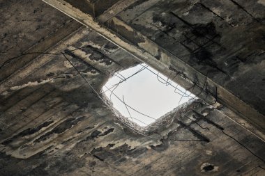 Tavanında bulutlu gökyüzüne bakan bir delik olan terk edilmiş, klasik bir çatı. Çökmüş beton duvar, terkedilmiş endüstriyel ya da konut binalarında delik var. Kapatın.