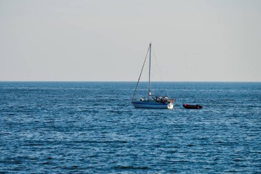 Mavi, sessiz denizde yüzen bir tekne, sakin bir hava, açık bir gökyüzü. Balıkçı teknesi ve motorlu teknesi olan güzel bir deniz manzarası. Güneşli bir günde yat, yaz macerası manzarası. Okyanus manzarası