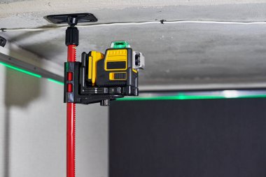 Tamamlanmamış dairede duvarda yeşil lazer ışını olan lazer seviyesi ölçüm aracı. Uzatma tavanı için profesyonel ekipman. Ev yenileme konsepti, kapatın.