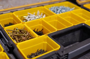 Küçük inşaat eşyalarıyla dolu sarı bir çanta. Vidalar, somunlar, civatalar, çiviler ve diğer aletleri atölyede bulunan inşaatçılarla dolu birçok depo kompartımanı. Düzenli ve düzenli.