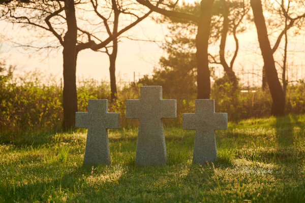 Three catholic stone crosses on green grass at sunset in German military cemetery in Europe. Memorial for dead soldiers of World War II in Baltiysk, Kaliningrad oblast, Russia