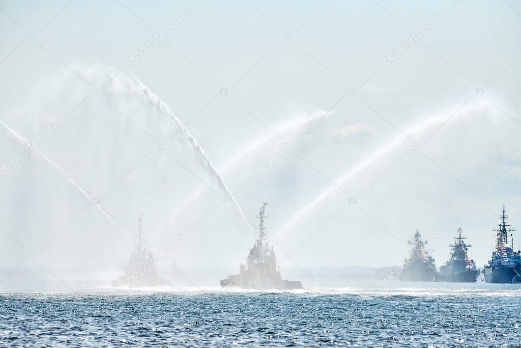 Floating tug boats spraying jets of water, demonstrating firefighting water cannons. Fire boats spraying foam with fire hoses. Offshore support vessels testing fire fighting jets