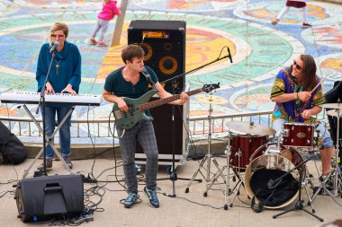 Svetlogorsk, Rusya - 08.14.2021 - açık hava festivalinde müzisyenler performans sergiliyor. Bas gitar, davul ve sentezleyici çalan sanatçılar sahnede şarkı söylüyorlar. İnsanlar için yaz sanatsal etkinlikleri kavramı