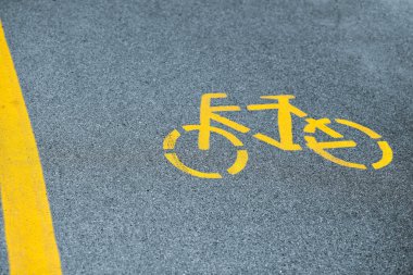 Bisiklet yolunda sarı bisiklet işareti, karayolu yakınında güvenli yol trafiği. Asfalt bisiklet yolundaki boyalı bisiklet yolu tabelası, yol güvenliği için sarı işaret.