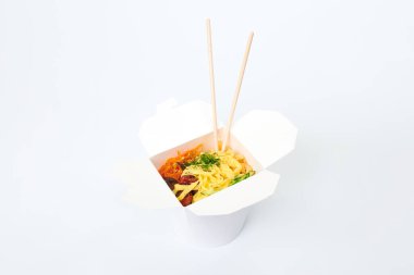 Beyaz kutuda deniz ürünleri ve sebzelerle pirinç tavası ve beyaz arka planda izole edilmiş ahşap yemek çubukları, yakın plan. Tava ve bambu çubuklarıyla paket servis kutusunu aç. Asya yemekleri, fast food teslimat konsepti