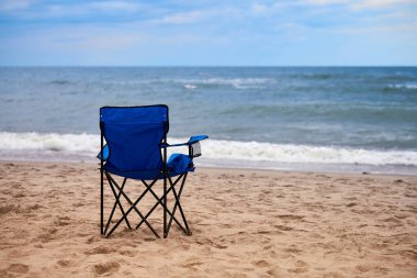 Deniz kıyısındaki mavi katlanır sandalye, deniz arka planında. Deniz sahilinde mavi sandalye, insansız. Sadece plaj tatili, Baltık Denizi sahilinde kimse, yalnızlık ve umutsuzluk.