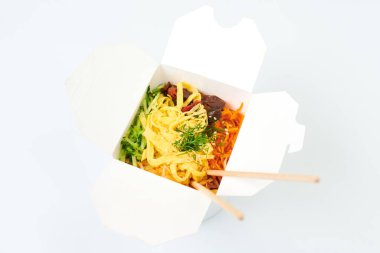 Beyaz kutuda deniz ürünleri ve sebzelerle pirinç tavası ve beyaz arka planda izole edilmiş ahşap yemek çubukları, stüdyo çekimi. Tava ve bambu çubuklarıyla paket servis kutusunu aç. Asya yemekleri, fast food teslimat konsepti