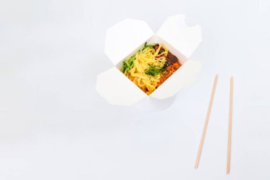 Beyaz kutuda deniz ürünleri ve sebzelerle pirinç tavası ve beyaz arka planda izole edilmiş ahşap yemek çubukları, kopyalama alanı. Tava ve bambu çubuklarıyla paket servis kutusunu aç. Asya yemekleri, fast food teslimat konsepti