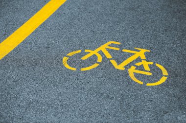 Bisiklet yolunda sarı bisiklet işareti, karayolu yakınında güvenli yol trafiği. Asfalt bisiklet yolundaki boyalı bisiklet yolu tabelası, yol güvenliği için sarı işaret.
