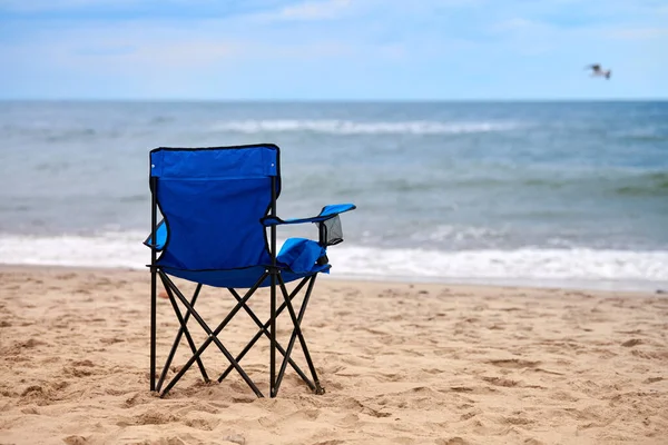 Blue folding chair back on seashore, sea background. Blue chair on sea beach, without people. Beach holiday alone, nobody on Baltic Sea beach, loneliness and hopelessness