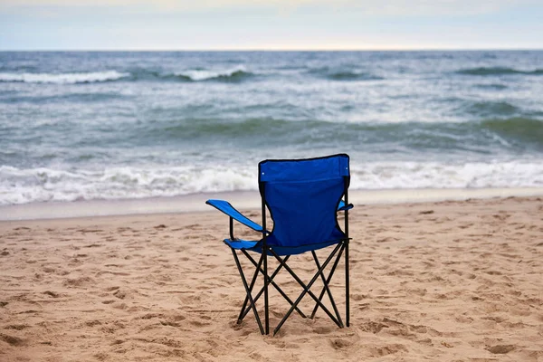 Blue folding chair back on seashore, sea background. Blue chair on sea beach, without people. Beach holiday alone, nobody on Baltic Sea beach, loneliness and hopelessness