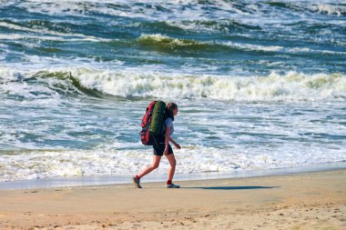 Baltiysk, Rusya - 07.30.2021 - denizde seyahat eden genç bir kadın. Büyük kırmızı sırt çantalı kız gezgin yeni bir bölgeyi keşfediyor, güzel Baltık Denizi geçmişi var. Tek başına kadın seyahati