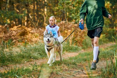 SVETLY, KALININGRAD OBLAST, RUSSIA - 2 Ekim 2021 - Canicross köpek ezme yarışı, genç erkek kardeş ve kız kardeşi Sibirya Husky köpeği, kızak köpek yarışı, açık havada koşan aile