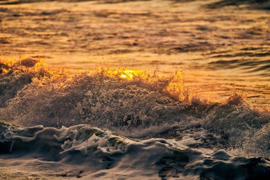 Renkli günbatımında atmosferik deniz köpüğü, altın rengi su kıvılcımları içinde açık deniz dalgalarının güzel manzarası. Deniz suyunun nefes kesici günbatımı, güzel deniz dalgaları, deniz kıyısından taze gelgit manzarası.