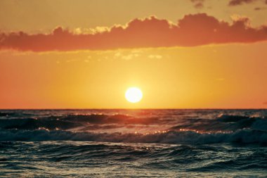 Sarı güneş derin mavi deniz dalgaları üzerinde ufuk çizgisine doğru iniyor. Gün batımında gün batımında gökyüzü manzaralı. Sonsuz deniz, sıcak güneş ışığında dramatik bir günbatımında. Güzel yaz deniz manzarası