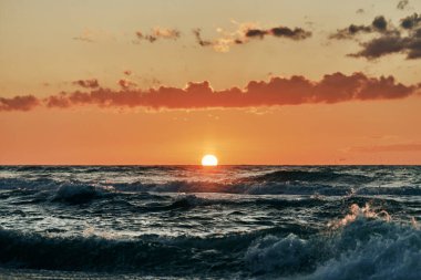 Mavi deniz dalgaları üzerinde yarım güneş, denizin üzerinde güzel gün batımı. Turkuaz deniz dalgaları dramatik güneş ışığı altında, gün batımında turuncu güneşten, atmosferik deniz dalgalarıyla nefes kesici deniz manzarası.